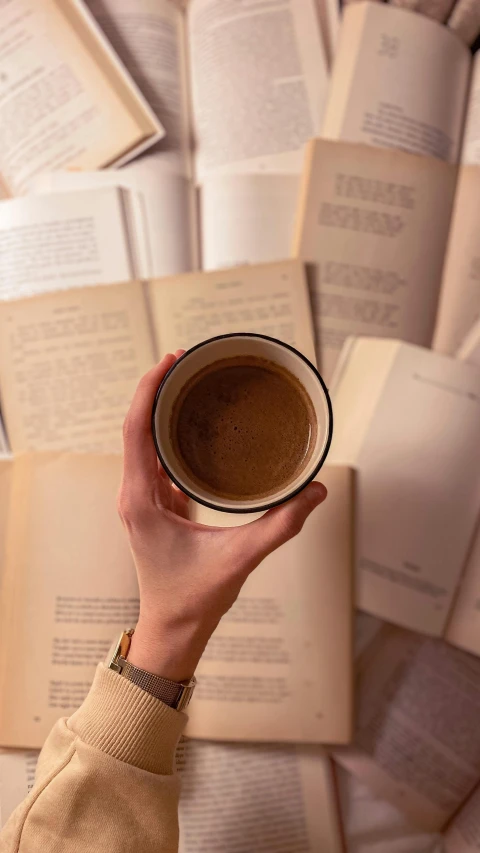 a hand holding up a mug of coffee and a stack of books