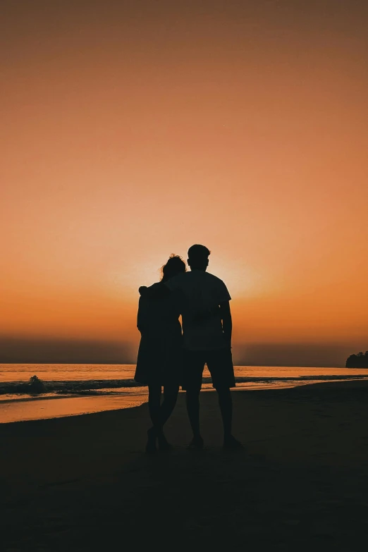 two people standing on top of a beach at sunset