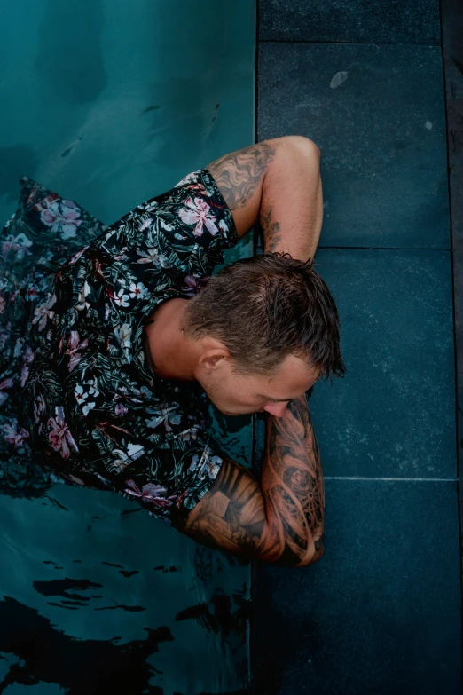 man with tattooed arms on wet ground near water