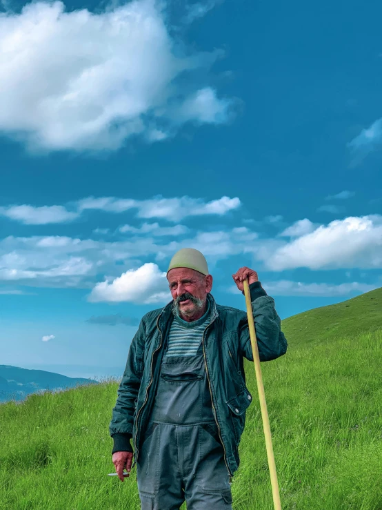 a man in overalls and a jacket on top of a grassy hill