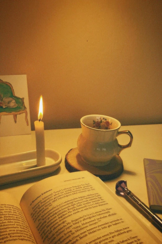 a table with an open book and cup and candle