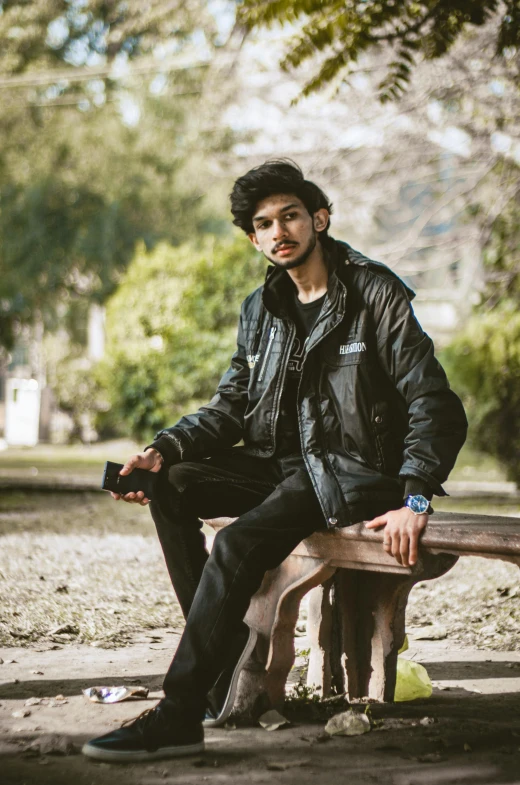 a young man in a black jacket sits on a bench