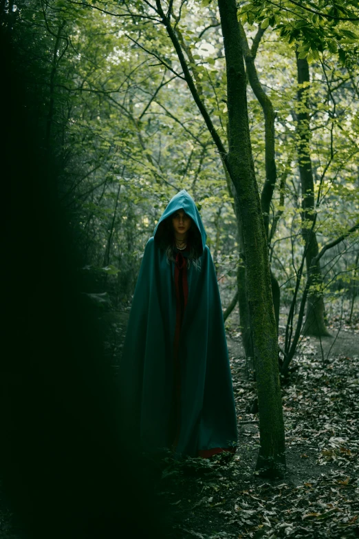 a woman wearing a hooded cape standing behind a tree