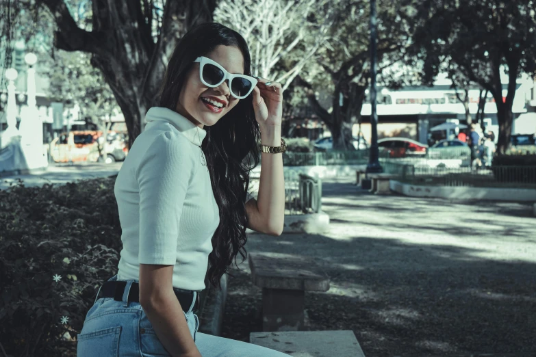 a girl wearing sunglasses and sitting on top of a park bench