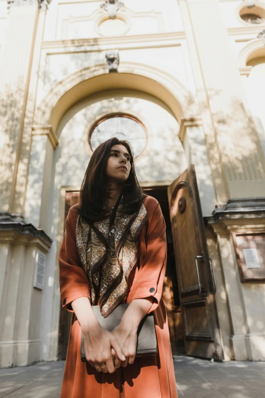 an asian woman standing outside of a church wearing a brown robe and holding her arms crossed