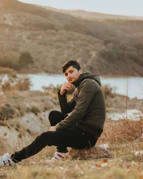 a man in a hoodie sitting near a river