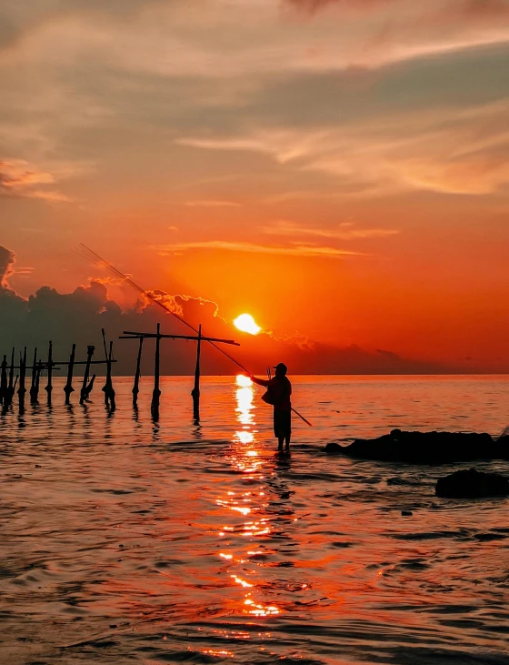 the sun sets on a calm ocean with a fisherman