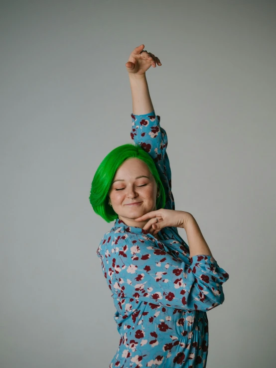 a woman with green hair and blue shirt posing with her arms raised