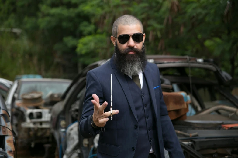 a bearded man with sunglasses is standing near cars