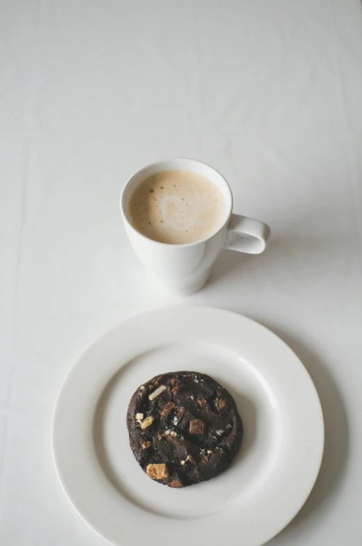 a white plate with a chocolate cookie next to a cup of coffee