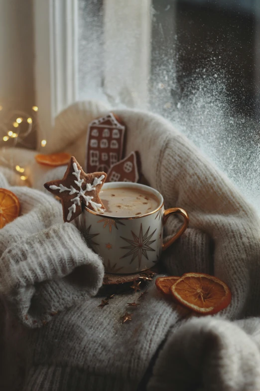 a mug filled with liquid and covered in a star cookie on top of a sweater next to christmas decorations