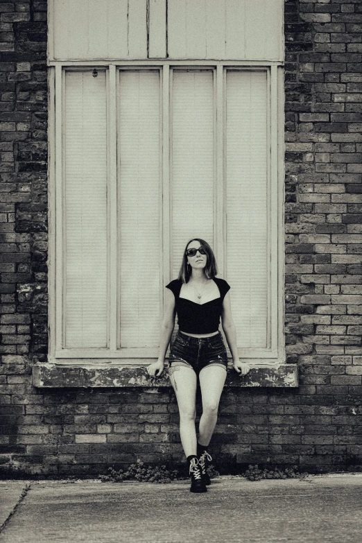 a young woman wearing short shorts is sitting next to a brick wall