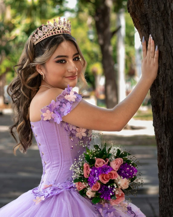  in purple dress and a floral bouquet holding her hand against a tree