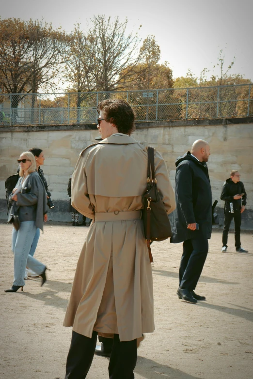 man in trench coat walking past people on sidewalk