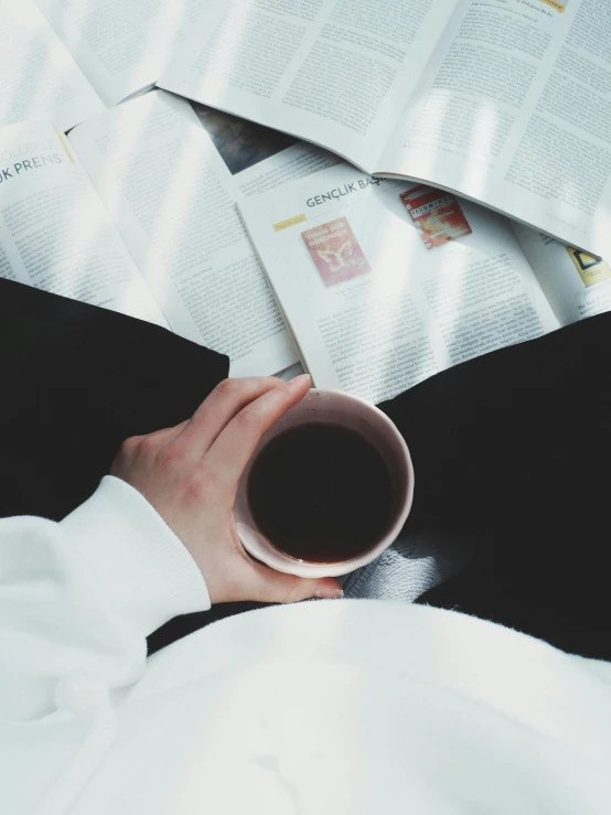 someone holding a cup with their hands over a pile of books