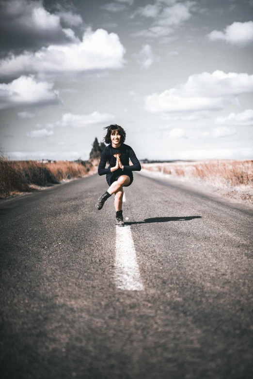 a girl is squatting on the side of an empty road