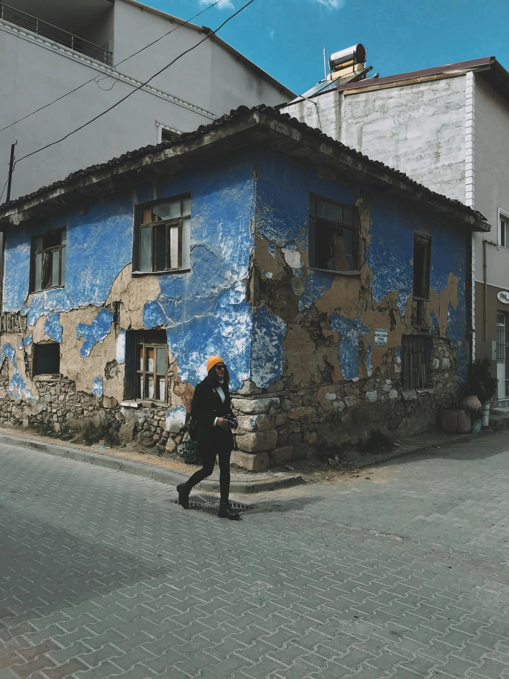 a woman walks on the side of an empty street in front of an old building with blue paint