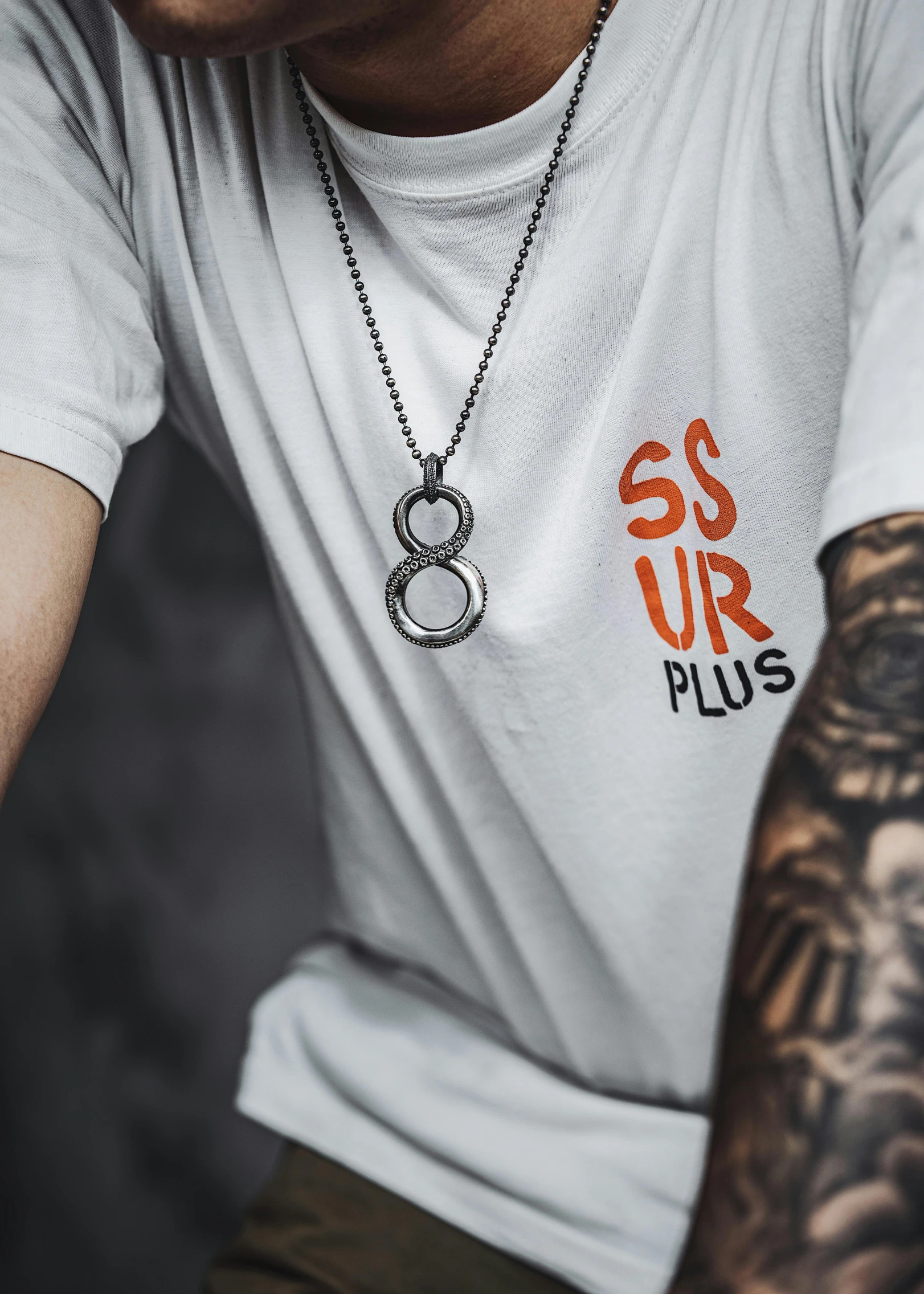 tattooed man in white shirt with necklace and a tattoo on his arm