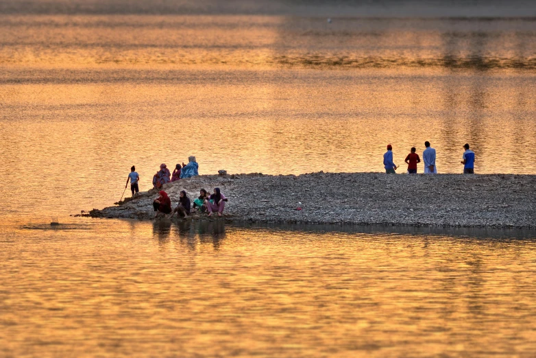 the sun is going down on the water and there are people walking in it