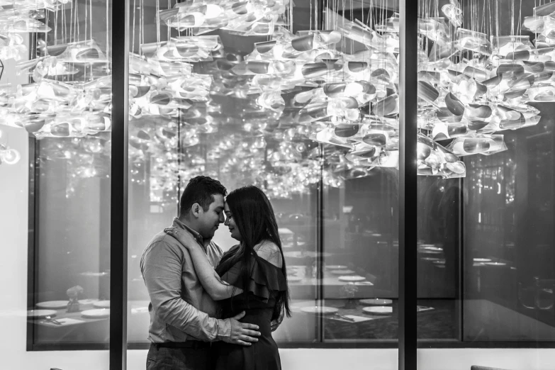 a man and woman hugging in front of the chandelier