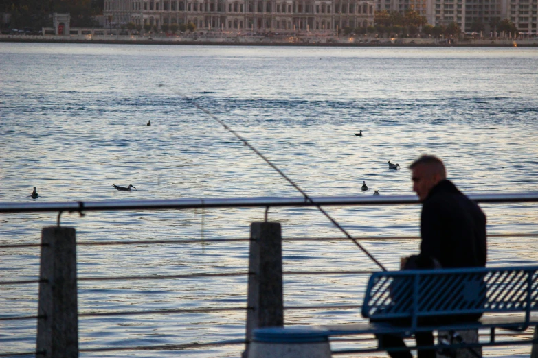 a man sits on the edge of a pier fishing