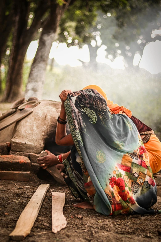 a woman working on soing sitting on the ground in front of trees