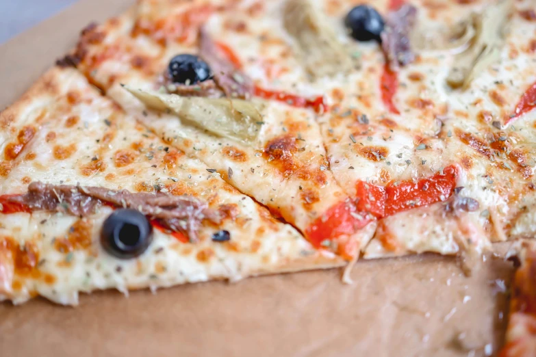 a sliced up pizza on a wooden plate with olives