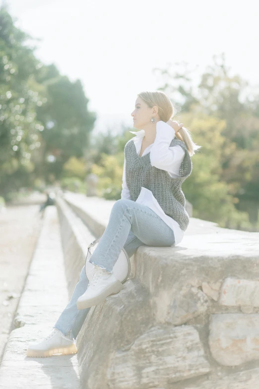 a woman is sitting on the top of a stone wall