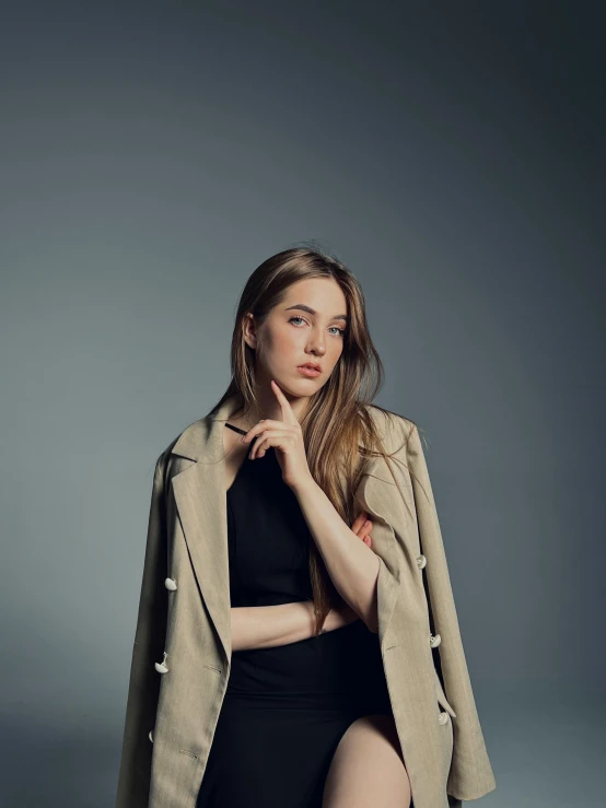 a woman posing in front of a grey background wearing a tan jacket