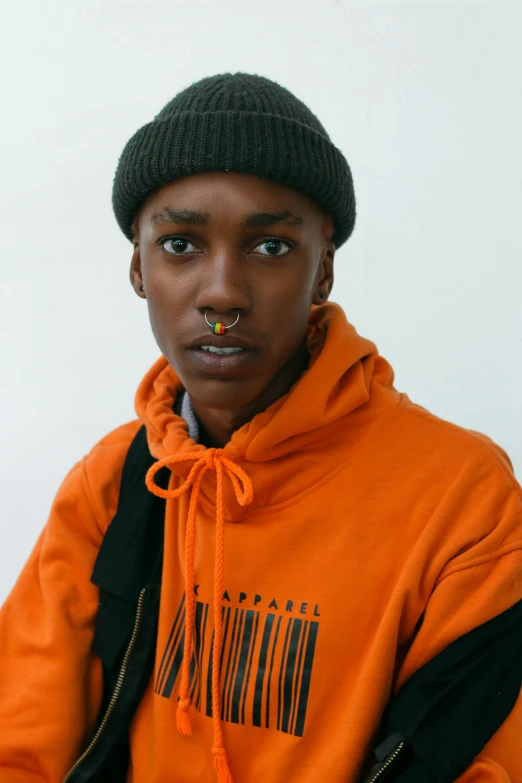 a black young man in an orange hoodie wearing a black and orange cap