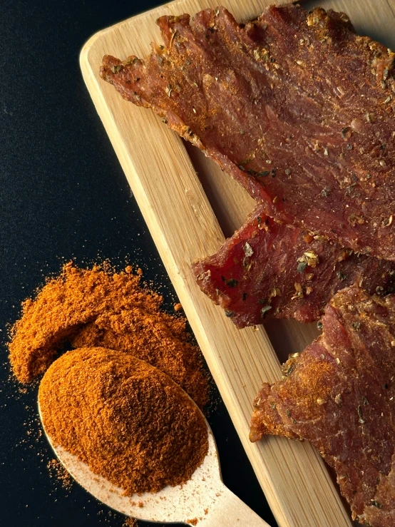 wooden spoon full of spices next to sliced steak on  board