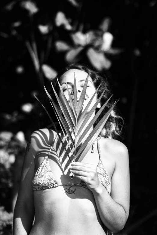 a woman in a bikini standing next to a tree and palm leaves