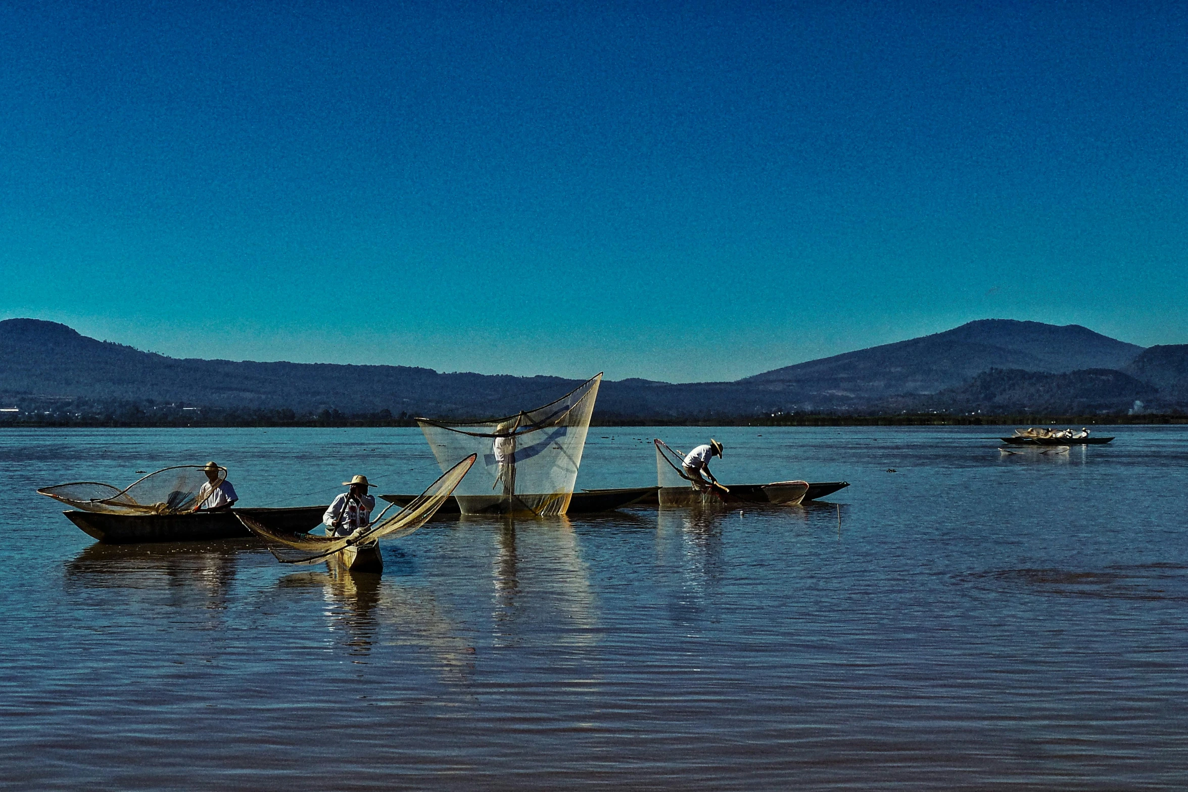 people standing in boats with fishing nets on water