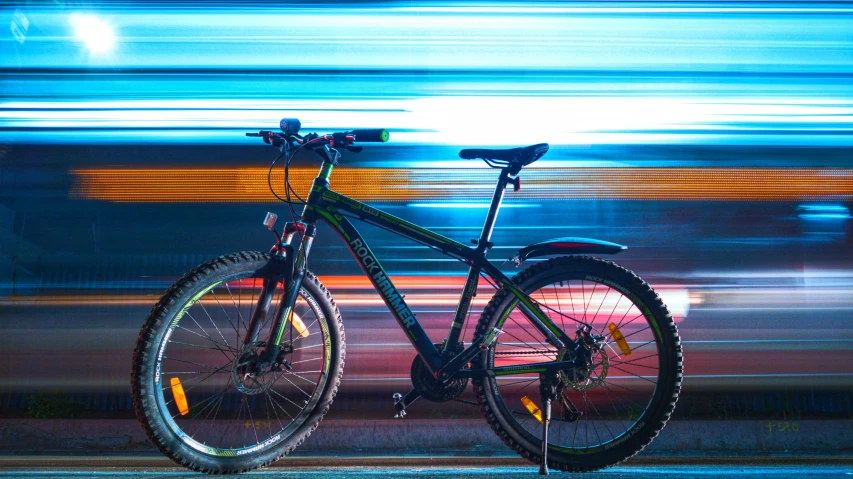 a bicycle parked at night with the bright lights of a train coming by