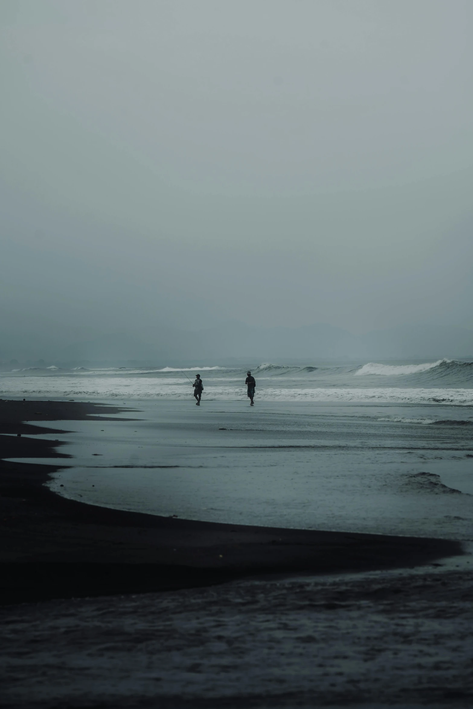 two people stand on a beach as waves crash onto the shore