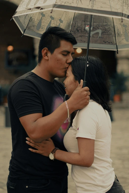 a man kisses the head of a woman under a clear umbrella