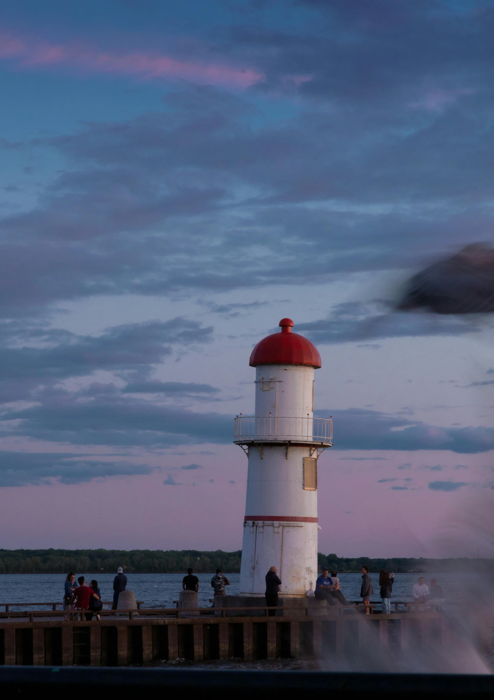 some people on the dock with a lighthouse and water in the background