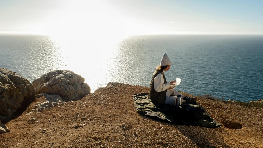 a woman is sitting on a blanket by the water