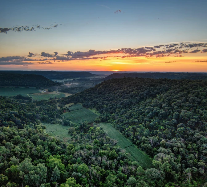 the sun sets over a valley with many trees