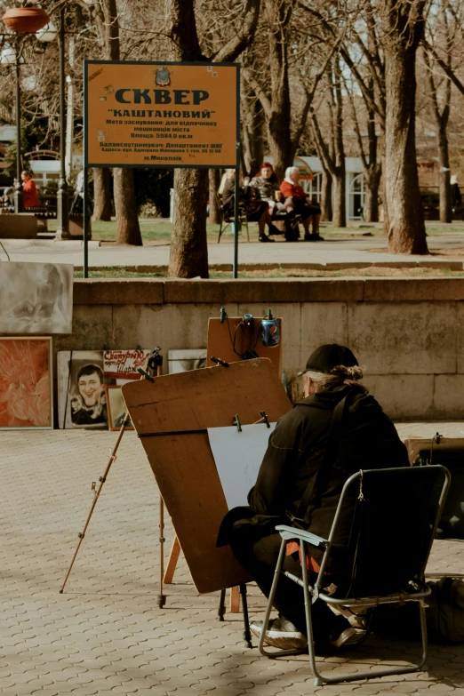 a man sitting down painting outside during the day