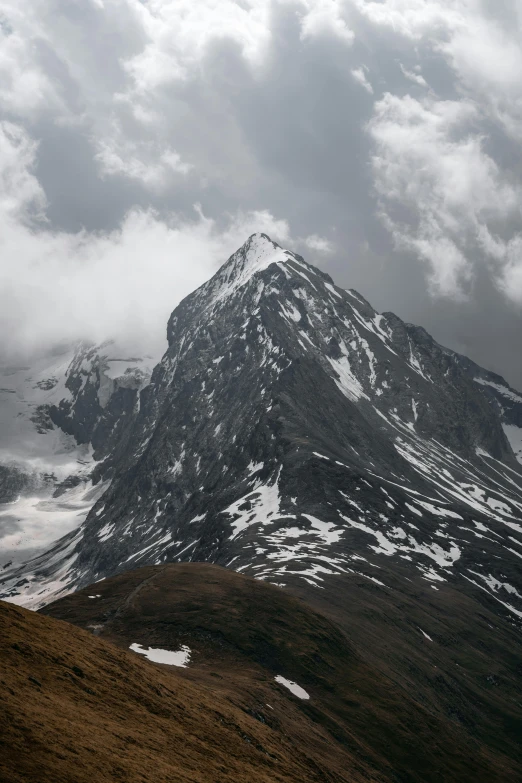 a lone bench sitting on the side of a mountain under cloudy skies