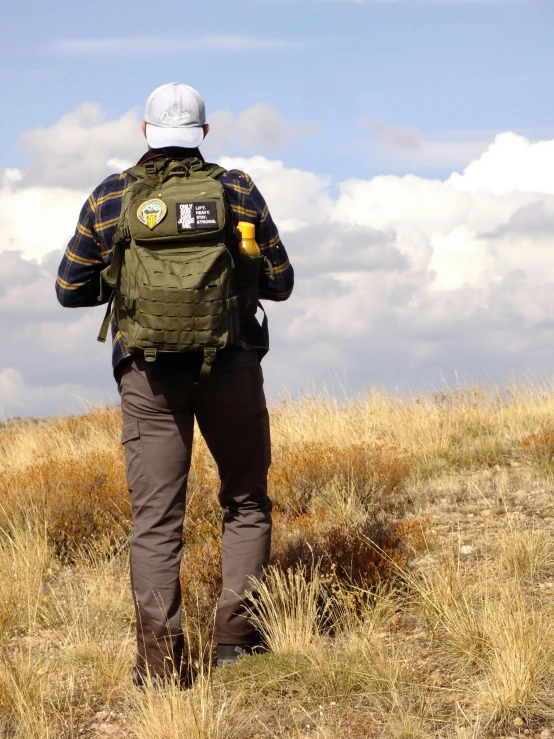 the backside of a man walking through the field with a backpack on