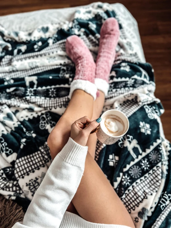 a girl in white sweater and pink mittens holding a coffee