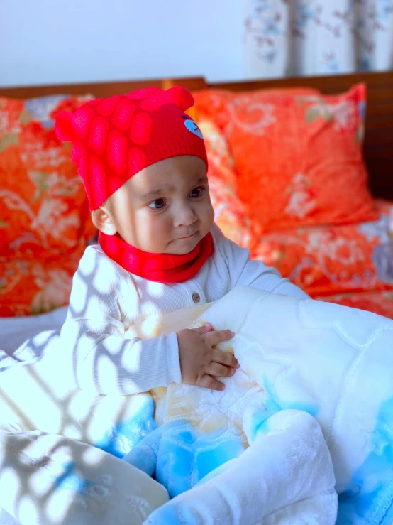 a child dressed in a red hat and sweater on a bed