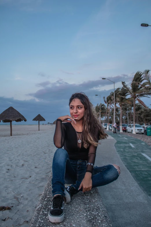 a young woman sitting on the sand by some umbrellas