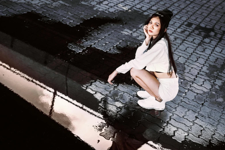 a beautiful young lady sitting next to water and brick sidewalk