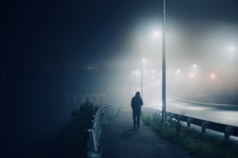 a man is walking down a sidewalk at night with fog