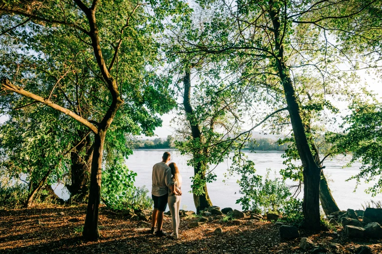 a couple stands by the waters edge under the trees