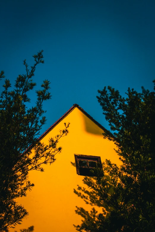 yellow building against a blue sky with small trees