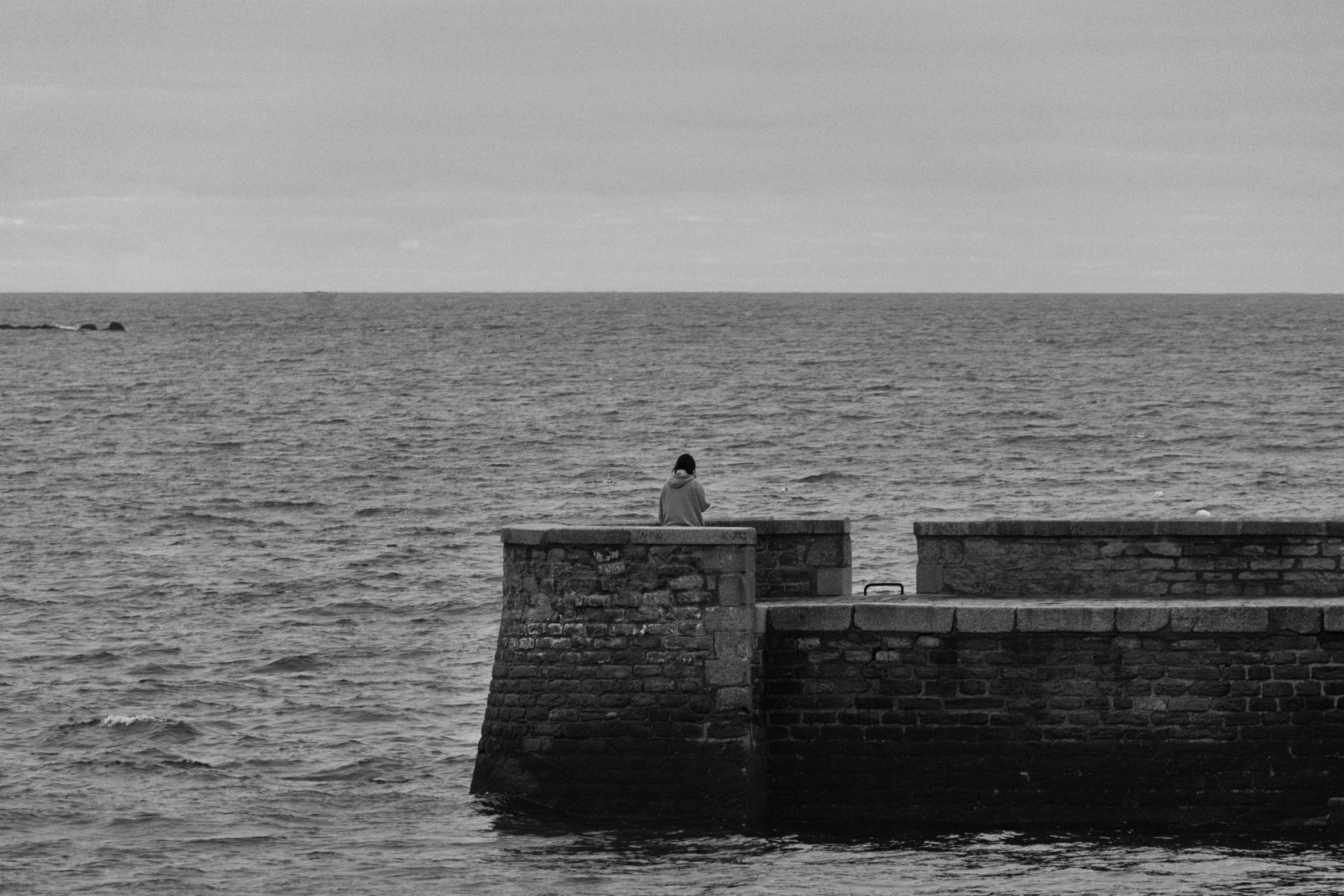 a black and white po of a person sitting on a brick wall